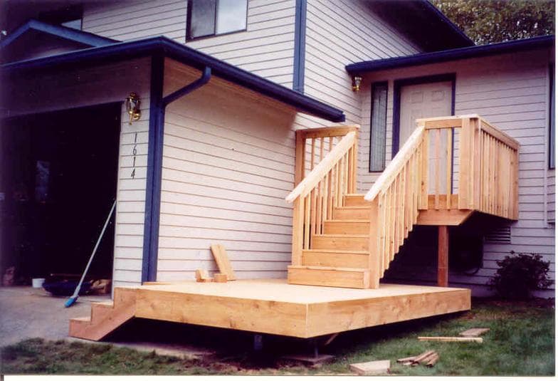 A newly built cedar deck with steps and railings against a two-storey home.