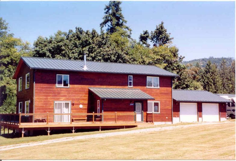 A finished Sing Square Log home with warm cedar siding and a charcoal standing-seam metal roof, under a clear sky with evergreens behind it.