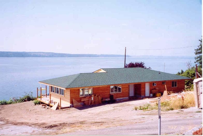 A home with its new green shingle roof complete, cedar siding below, the water beyond.